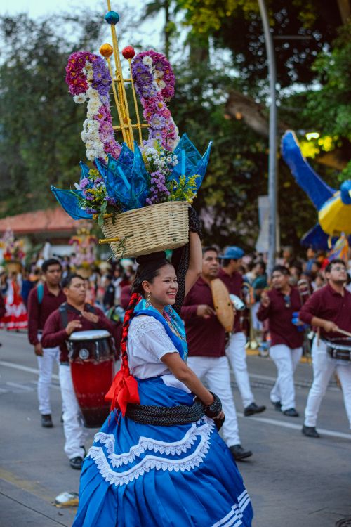 Free A lively festival parade featuring a woman in a blue dress carrying a floral basket. Stock Photo