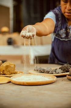 Close-up of a woman sifting flour onto a table in a rustic kitchen setting, showcasing traditional cooking methods.