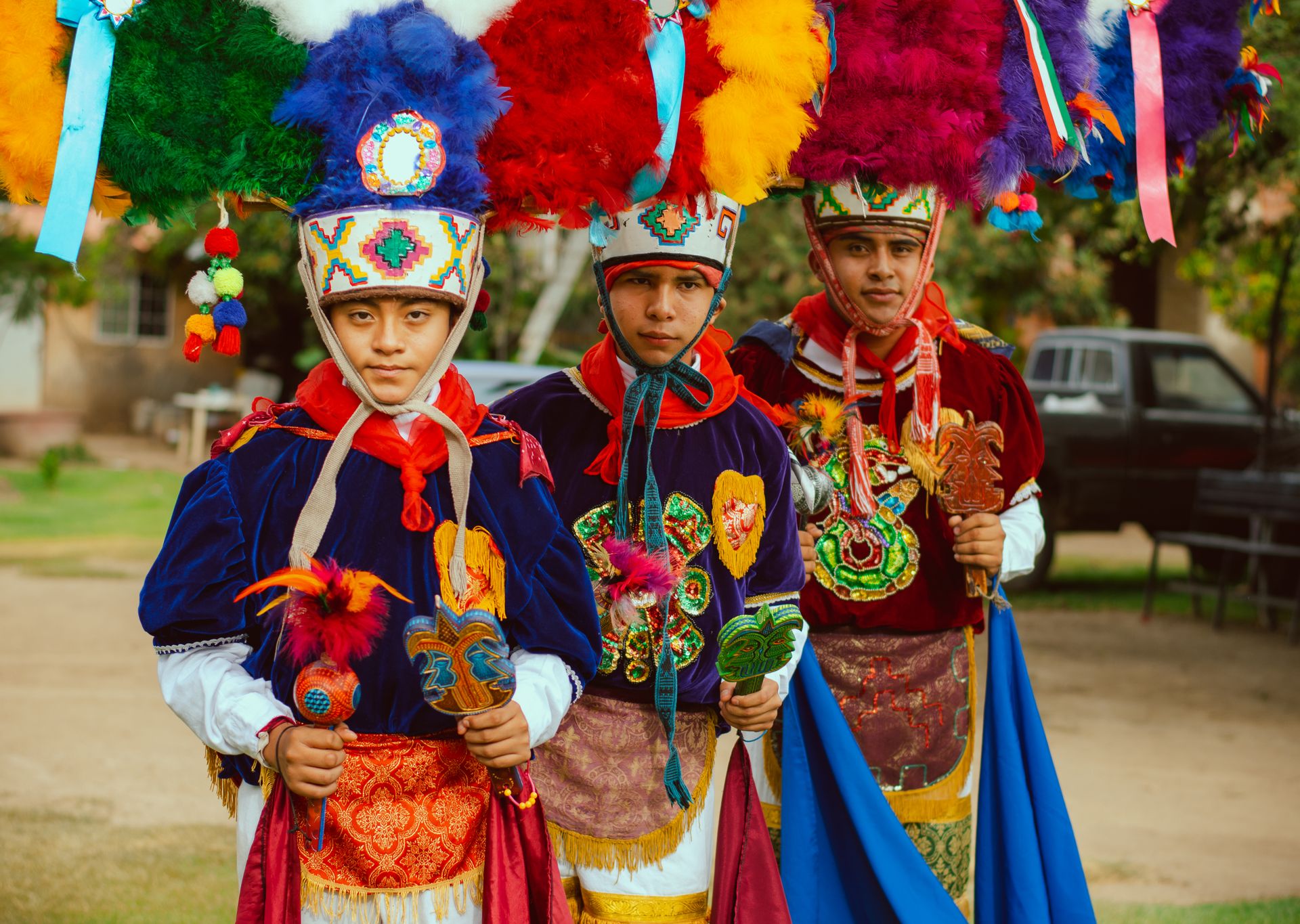 Three men in colorful traditional Mexican costumes with feathered hats and embroidered designs.