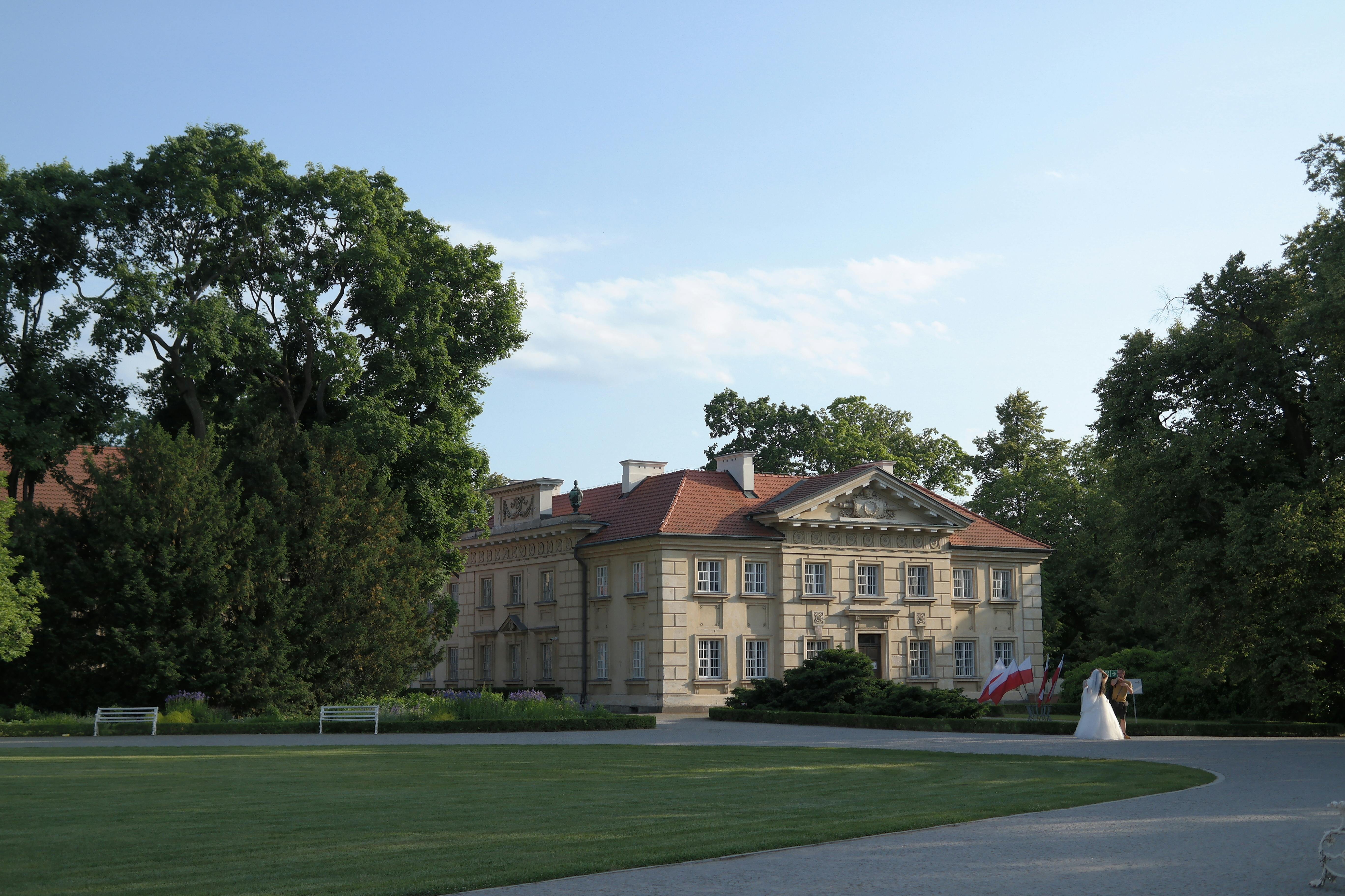 A beautiful mansion surrounded by gardens with a couple in wedding attire.