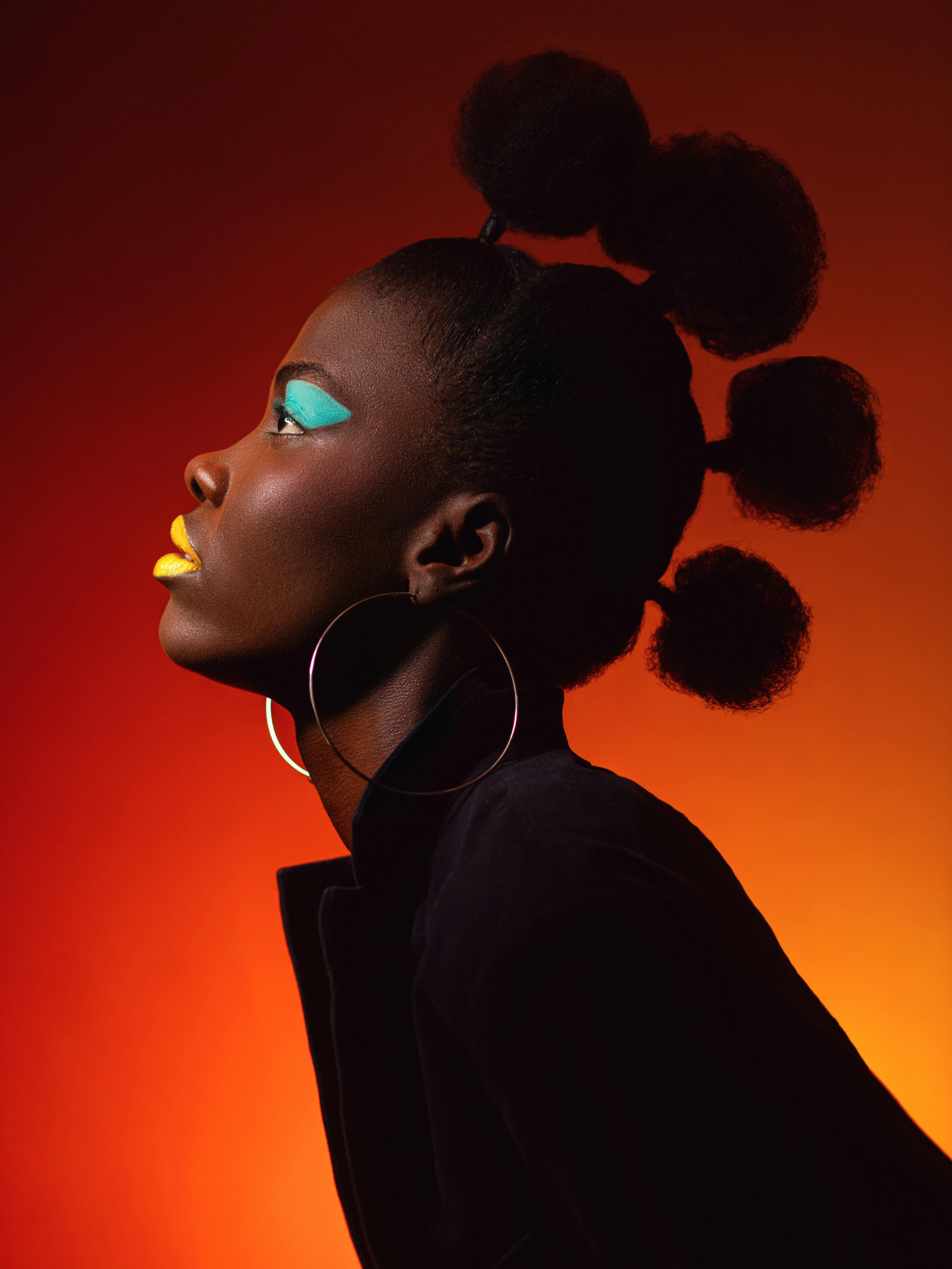 Striking portrait of a woman with colorful makeup and unique afro hairstyle on a vivid gradient background.