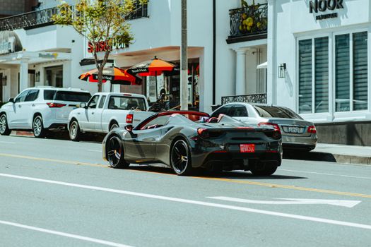 Sleek black sports car cruising through a vibrant city street with upscale shops.