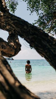 Woman in a swimsuit stands in the ocean surrounded by tropical scenery.