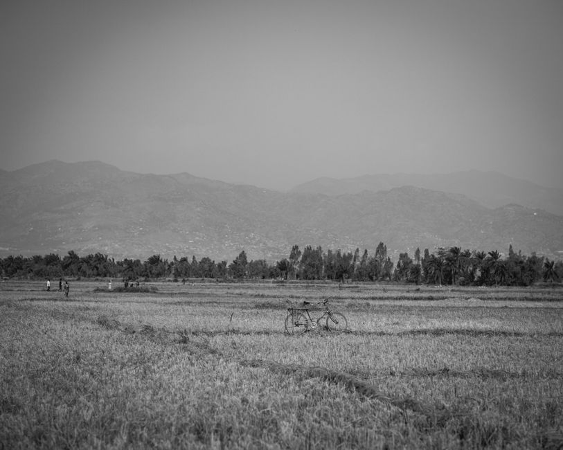 Black and white rural landscape in Burundi featuring a bicycle, farmland, and distant hills.