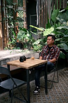 Young man enjoys a sunny day in a lush green outdoor cafe setting.