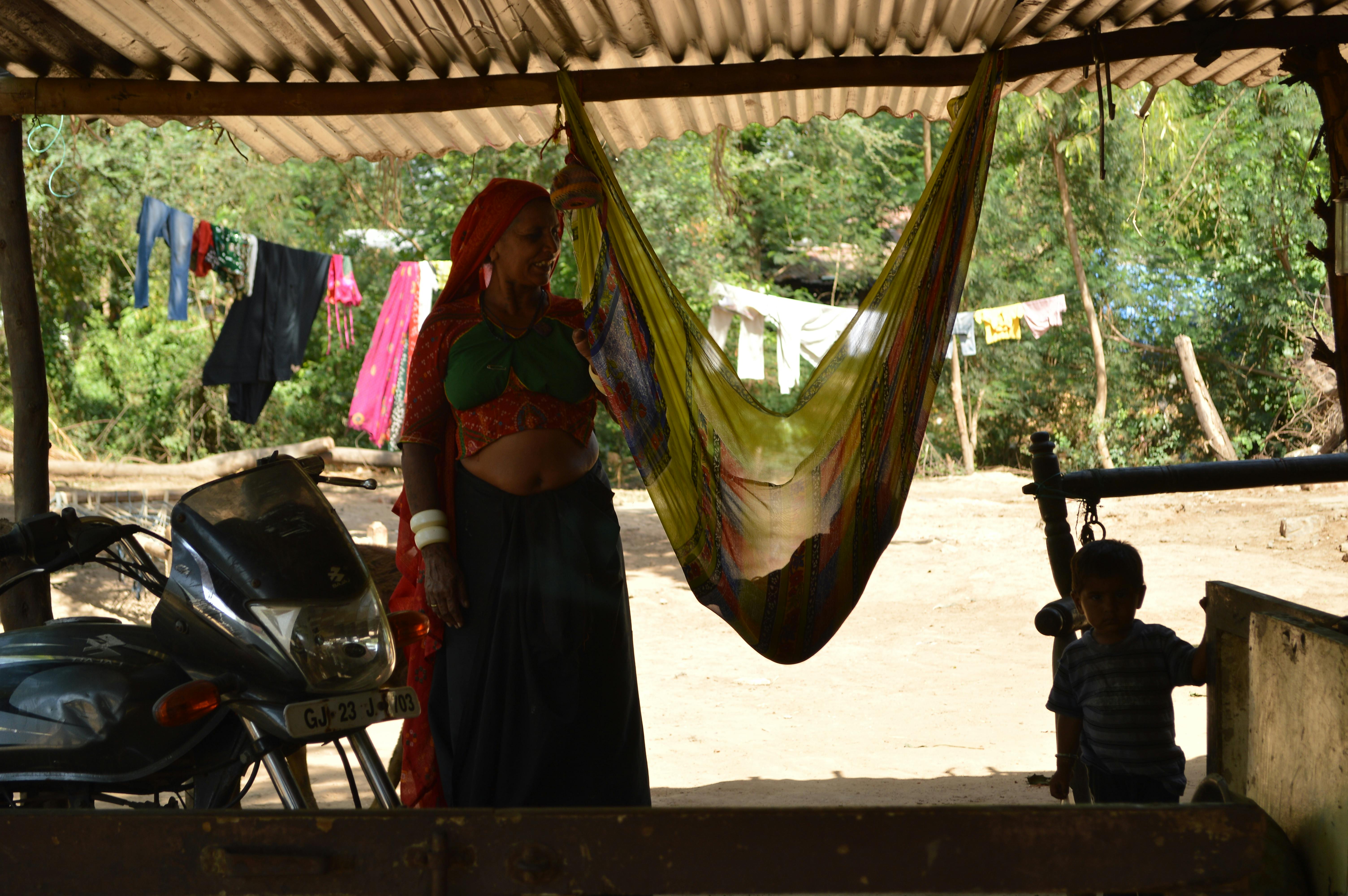 A rural woman and child with a colorful hammock in a traditional outdoor setting.