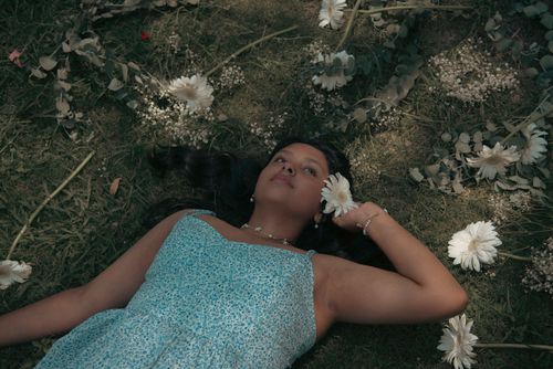 Free A woman in a blue dress lies among flowers on a sunny day, creating a serene, dreamy atmosphere. Stock Photo