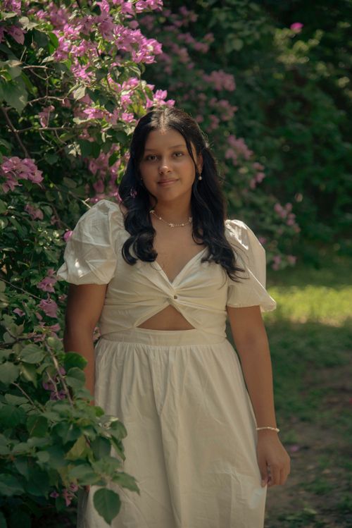 Free Portrait of a young woman in a white dress surrounded by pink flowers on a sunny day. Stock Photo