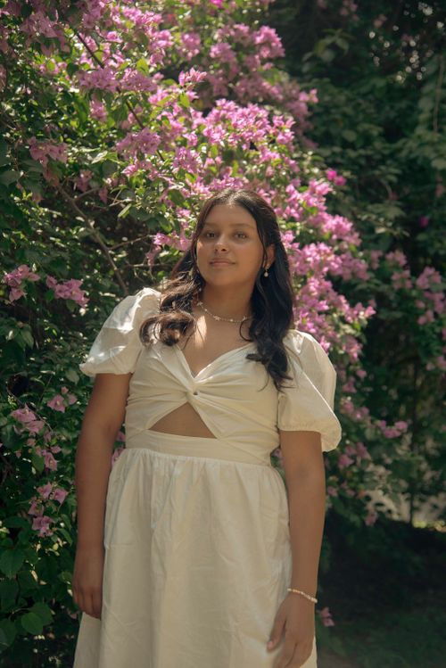 Free Portrait of a young woman in a white dress standing by a lush flowering bush outdoors. Stock Photo