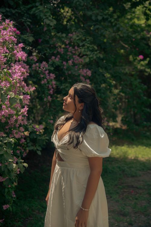 Free A serene outdoor portrait of a young woman in a white dress by blooming flowers. Stock Photo