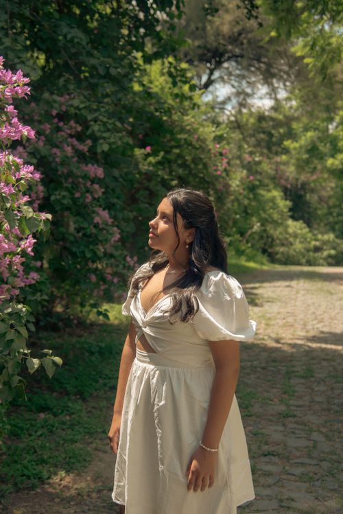 Free Young woman in a white dress standing on a garden path surrounded by nature. Stock Photo