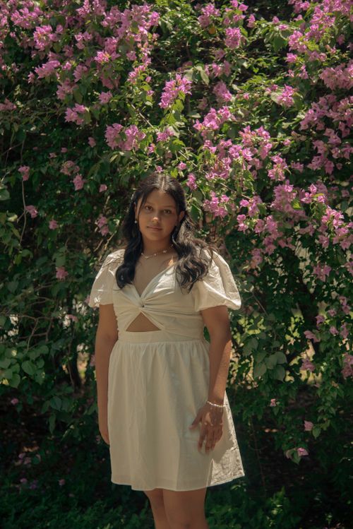 Free A woman stands in a white dress in front of a lush pink bougainvillea bush outdoors. Stock Photo