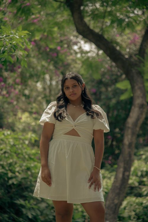 Free A woman in a white dress poses confidently outdoors surrounded by lush greenery. Stock Photo