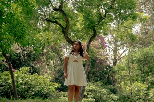 Free A woman in a white dress stands amidst lush greenery and vibrant flowers during the day. Stock Photo