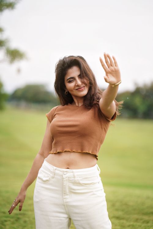 Free Woman smiling outdoors, enjoying a sunny day with a hand raised towards the camera. Stock Photo