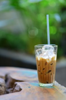Close-up of iced coffee in a glass with ice cubes on a rustic wooden table, outdoors.