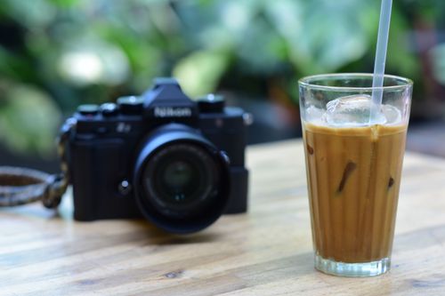 Free Glass of iced coffee with camera on a wooden table, perfect for a refreshing break. Stock Photo