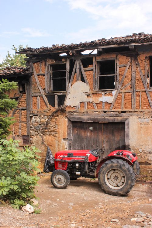 Free Red tractor parked next to a weathered old farmhouse, rustic charm. Stock Photo
