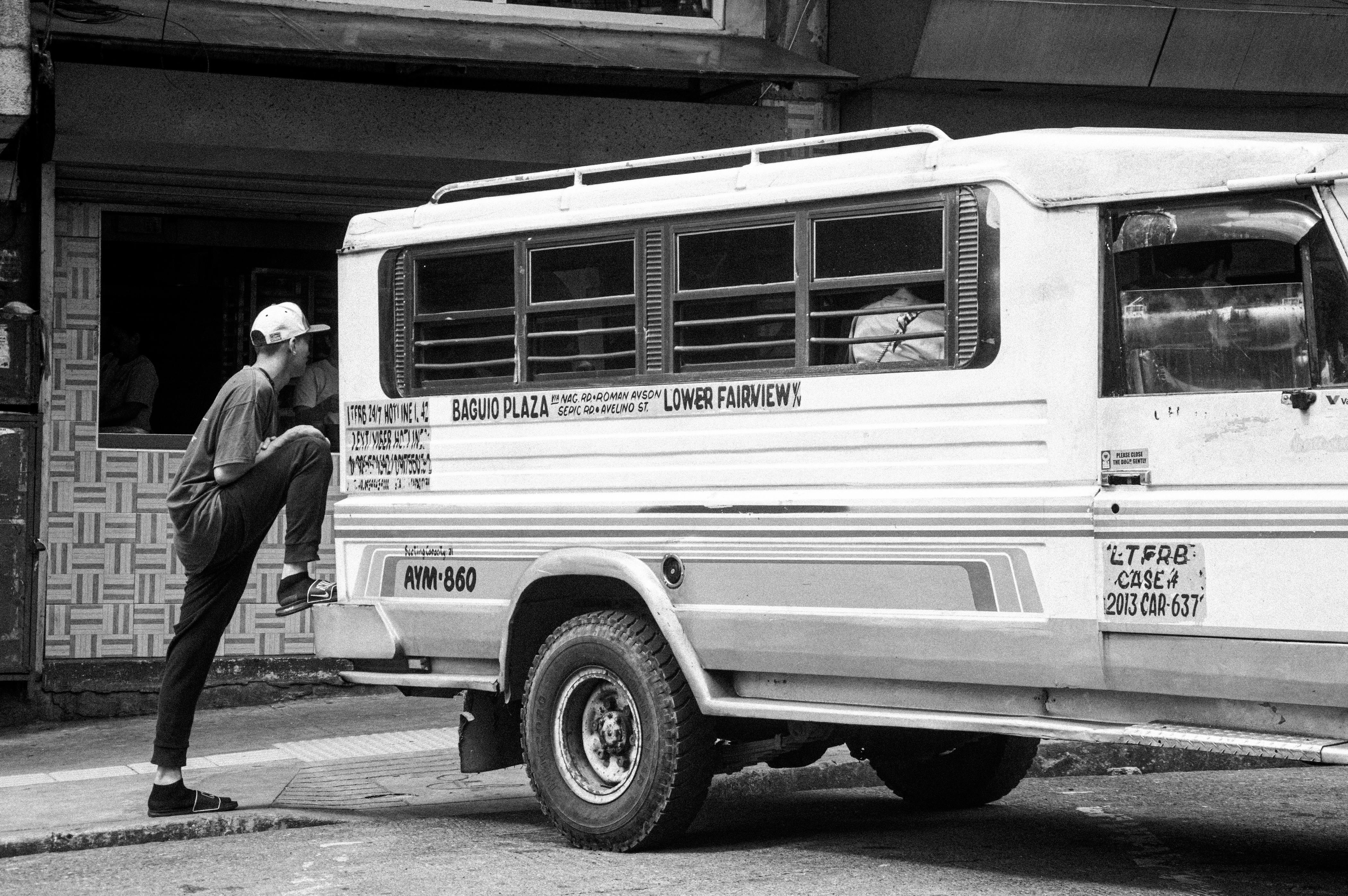 Free Black and white photo of a man boarding a jeepney at an urban street corner. Stock Photo