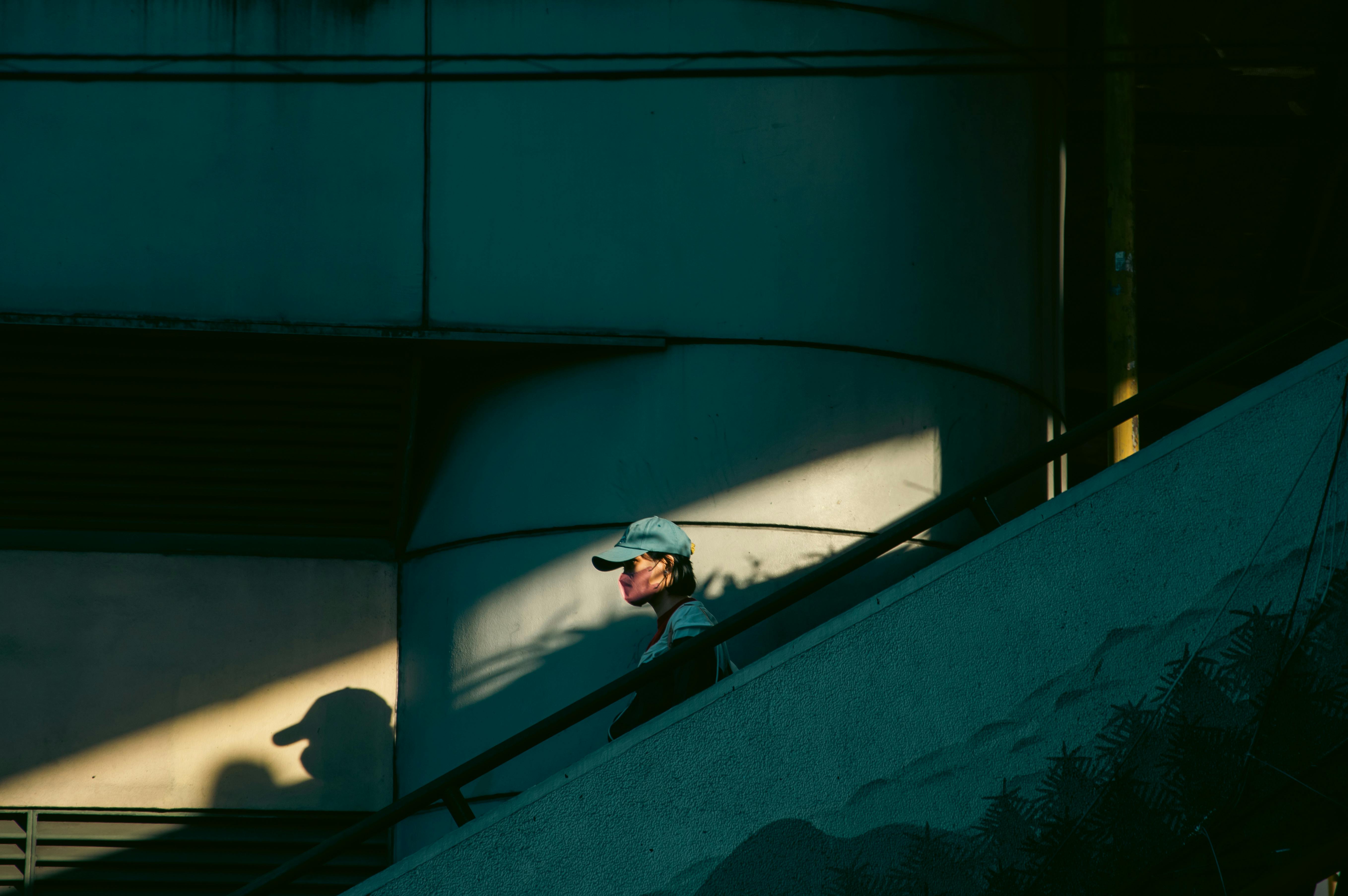 Dramatic lighting captures an adult man with a cap ascending stairs in a cityscape.