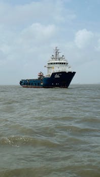 A blue cargo ship sailing through the open sea under a cloudy, overcast sky.