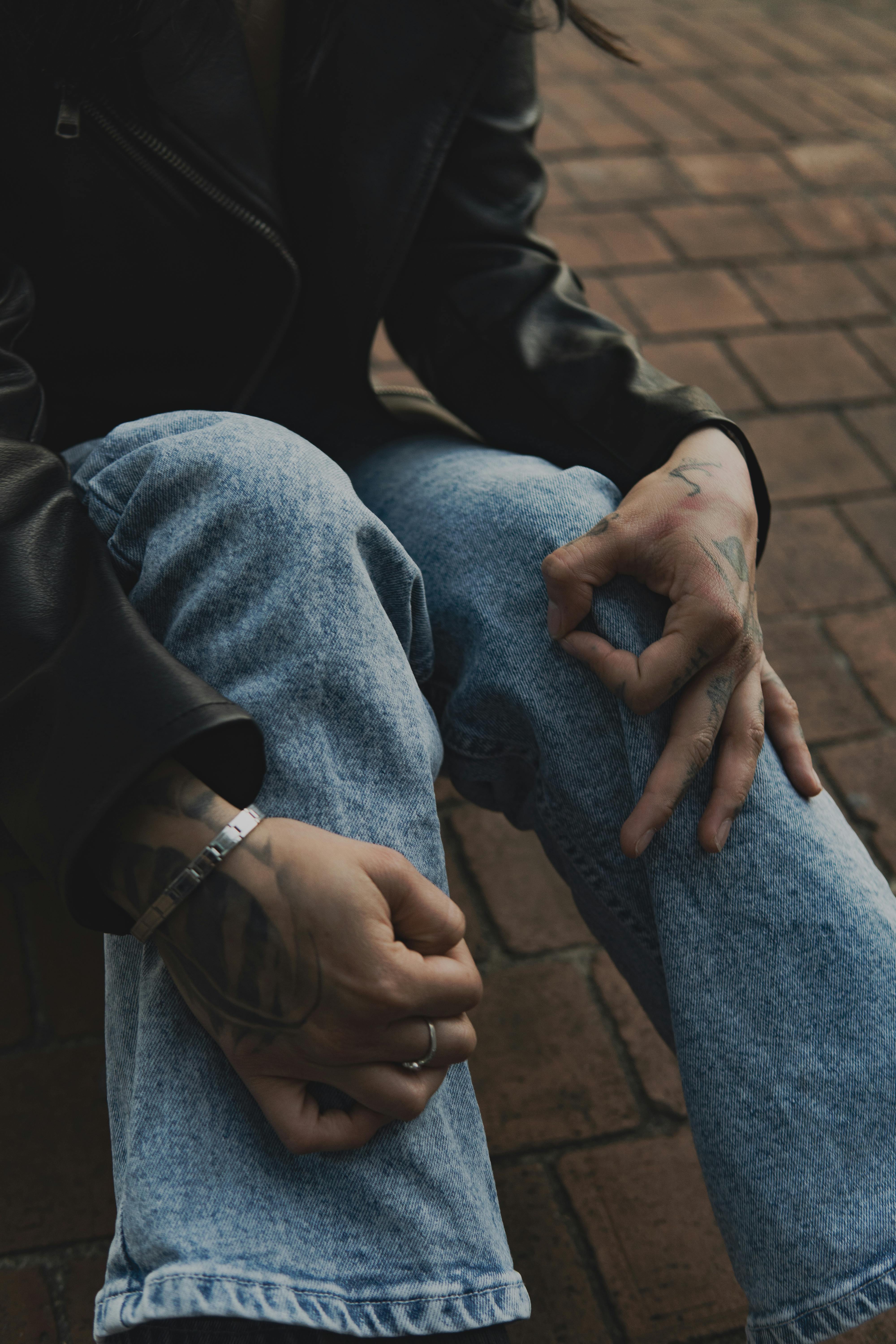 무료 데님과 가죽옷을 입고 벽돌길에 앉아 있는 문신이 있는 사람의 클로즈업. 스톡 사진