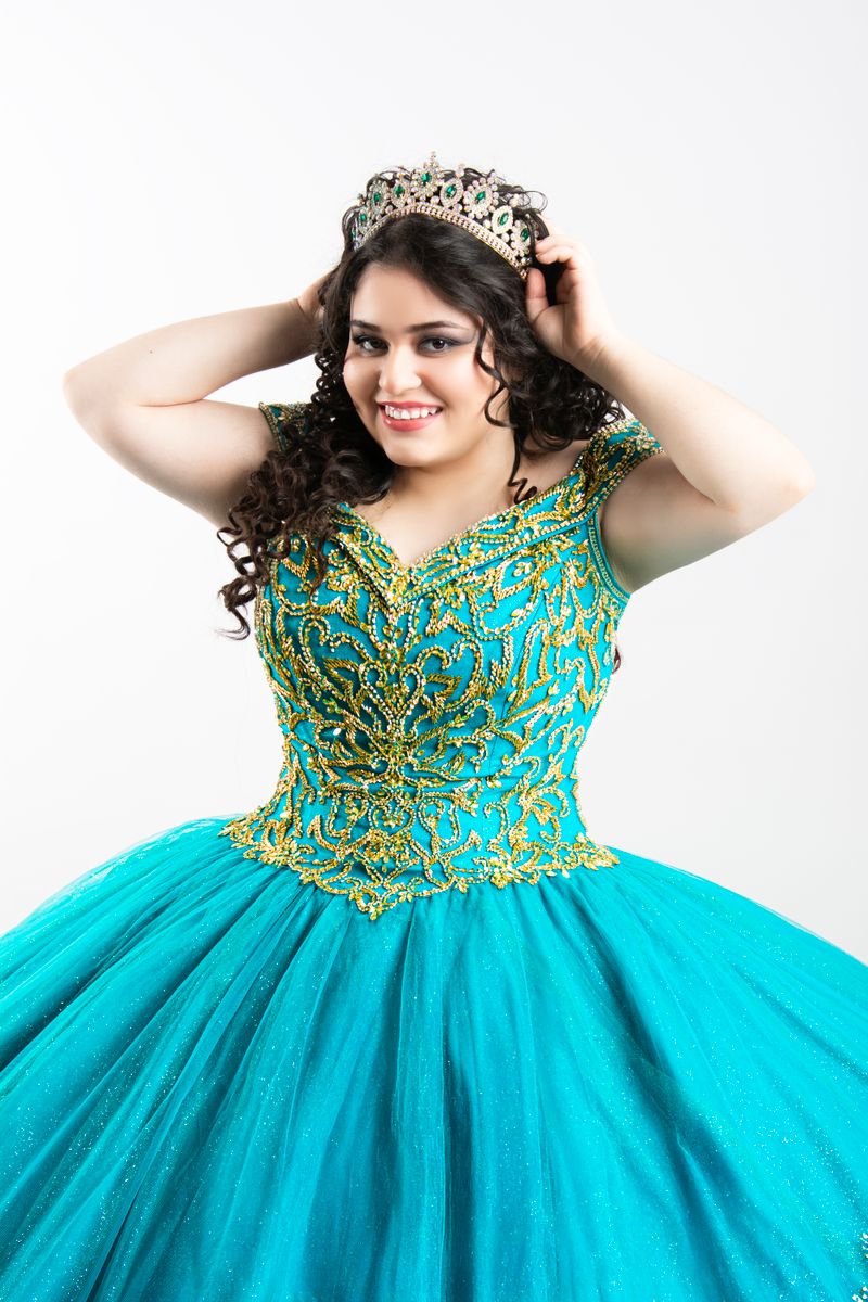 A young woman in an embellished turquoise gown adjusts her tiara, exuding elegance and charm.