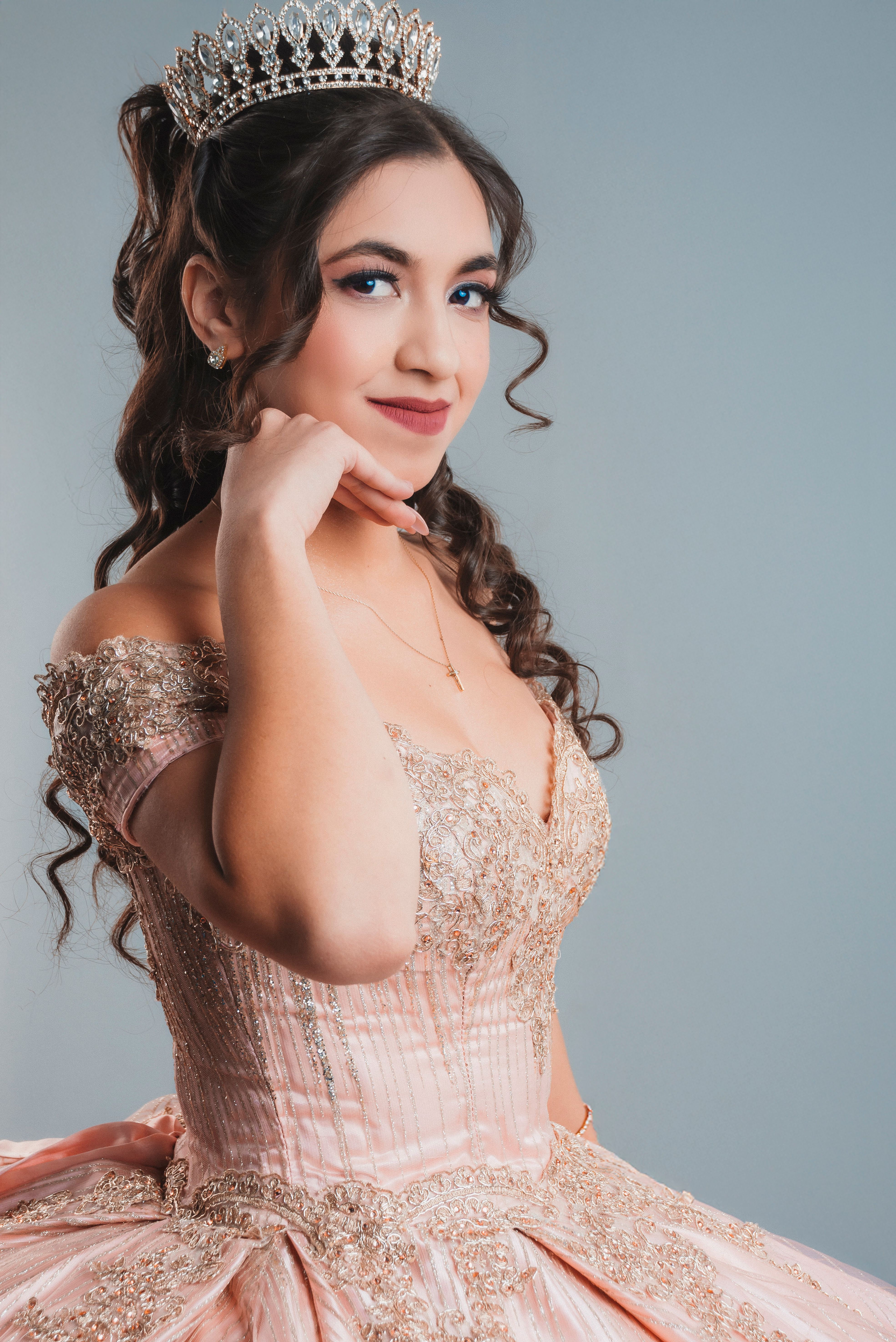 Portrait of a young woman in a stunning pink gown and tiara, exuding elegance.