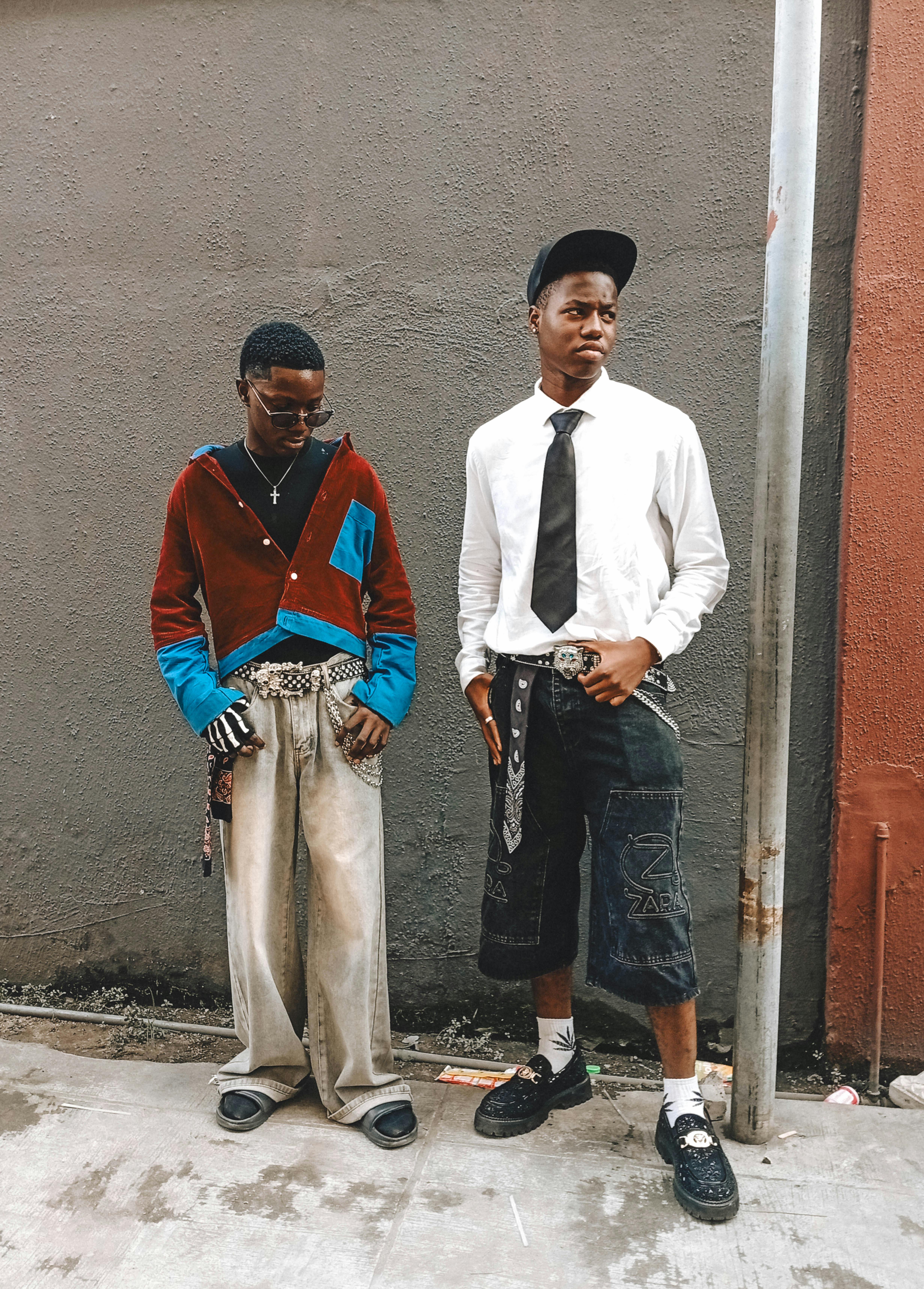 Two stylish young adults pose in urban streetwear against a city backdrop.