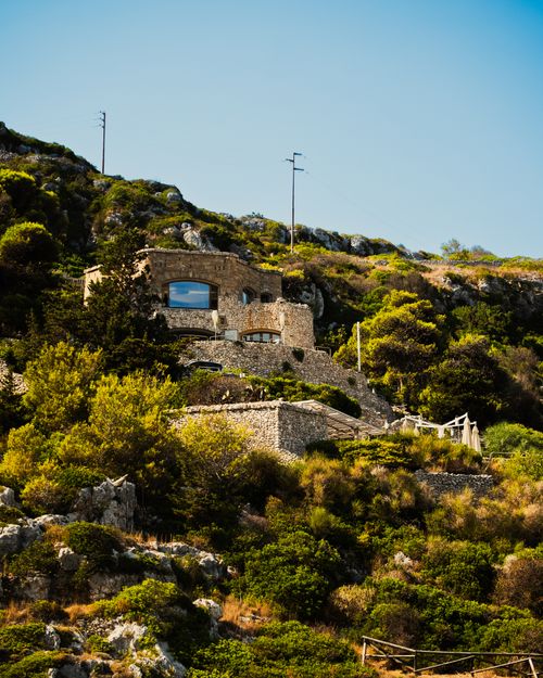 Free Charming stone house nestled in lush hillside greenery under a bright blue sky. Stock Photo