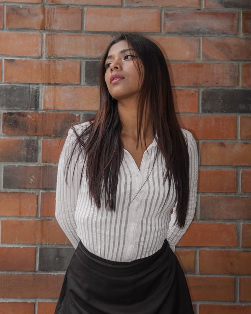 Free A young woman in a stylish outfit poses confidently against a textured brick wall. Stock Photo