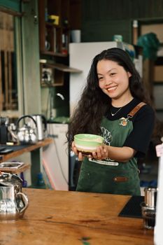 A cheerful young barista holding a latte bowl in a cozy cafe setting.