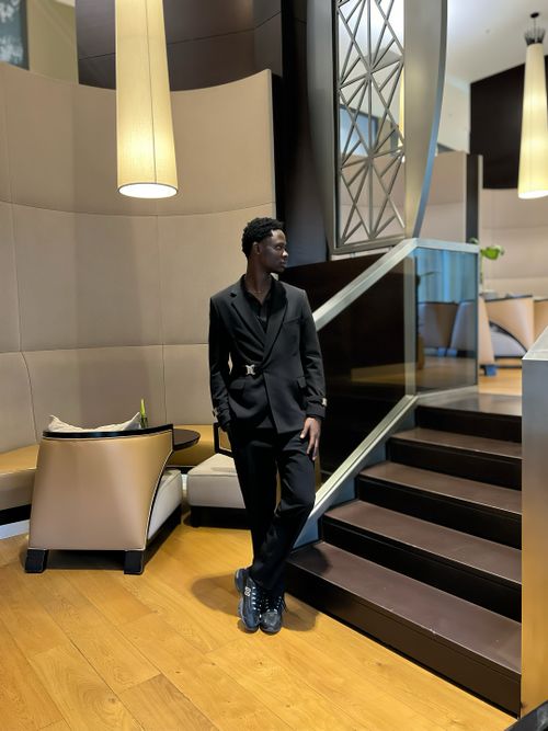 Free Stylish man in a black suit standing in a sophisticated hotel lobby with modern decor. Stock Photo