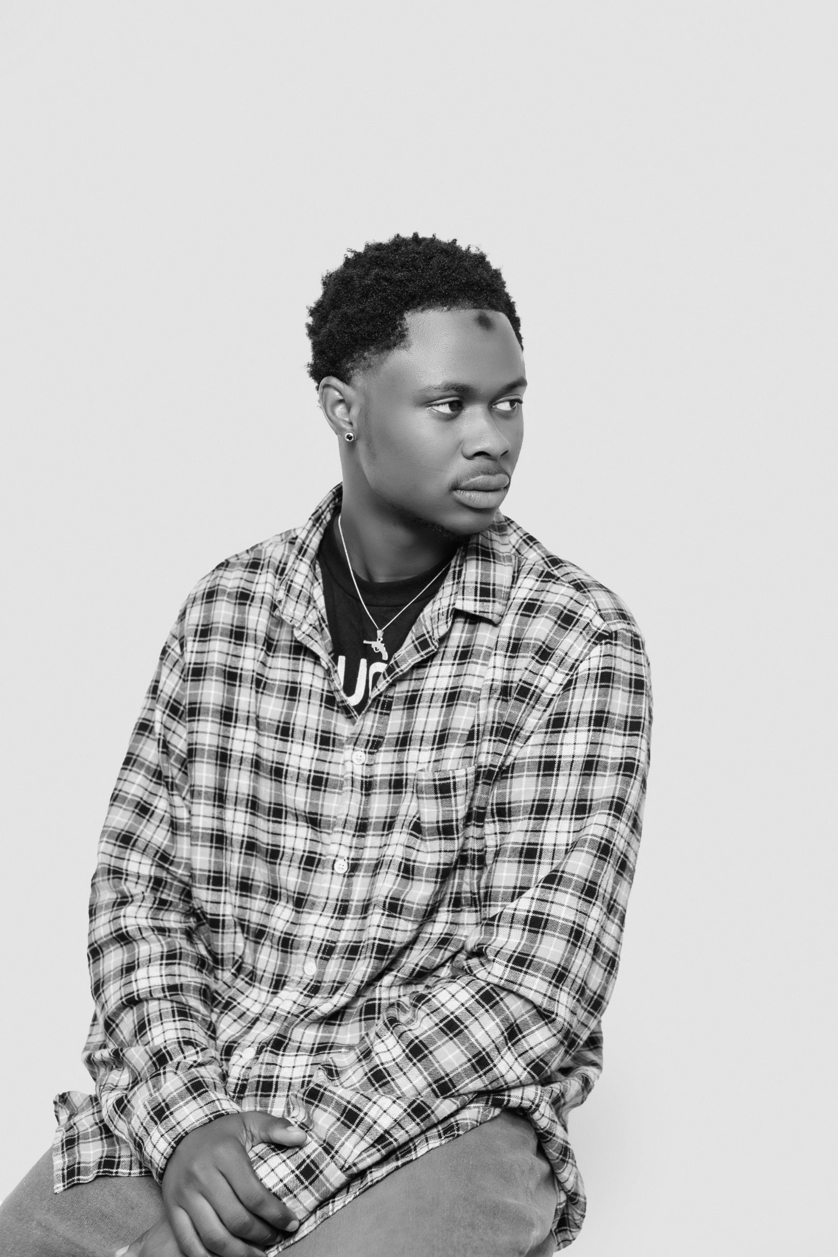Monochrome portrait of a young man wearing a plaid shirt, looking aside with a neutral expression.