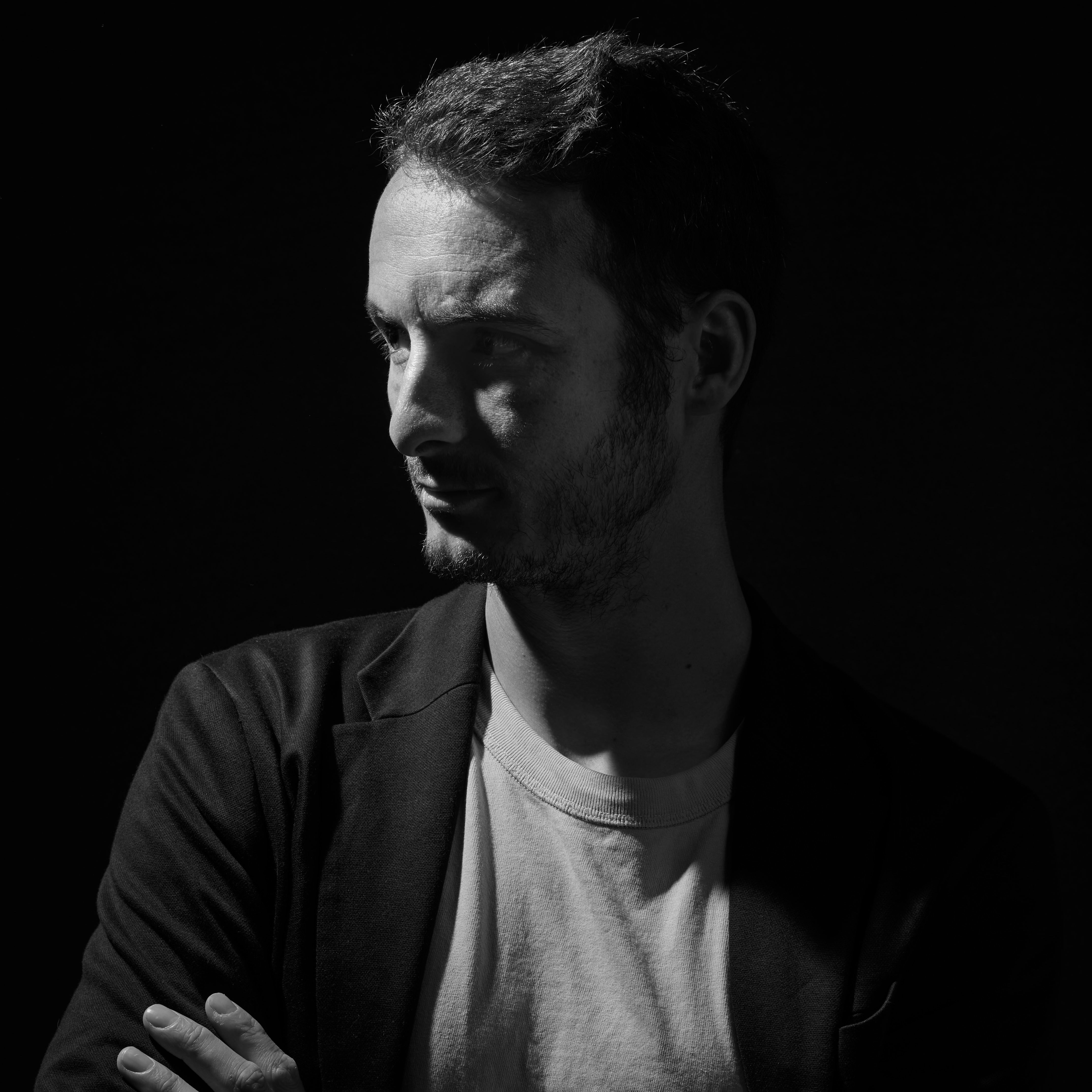 Dramatic side-lit black and white portrait of a man in a studio setting.