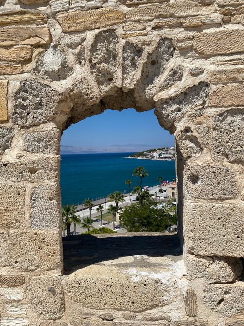 Free Ancient stone archway frames a vibrant blue seascape and coastal town. Stock Photo