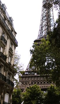 Charming view of the Eiffel Tower framed by classic Parisian architecture and lush greenery.