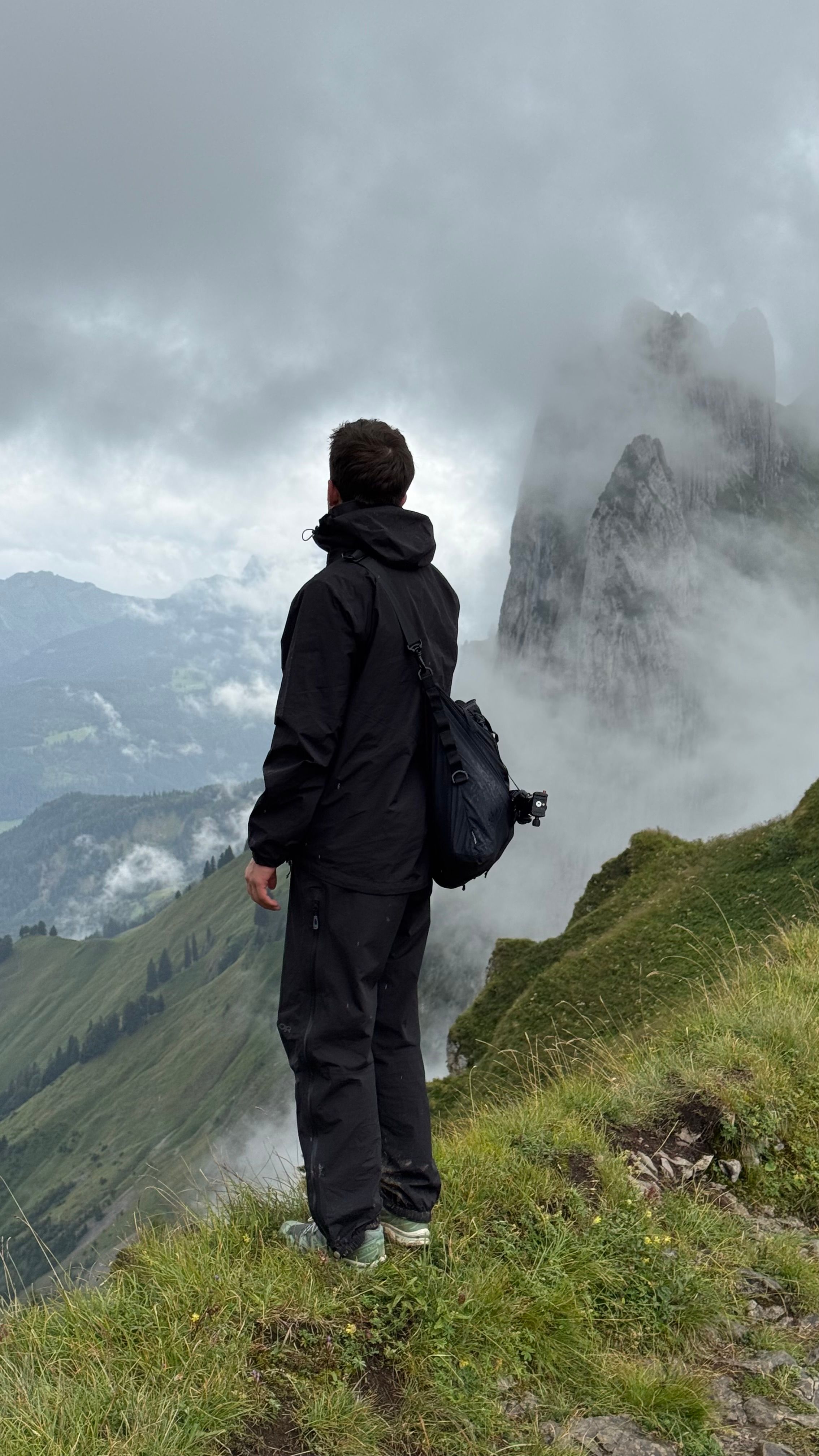A solitary hiker stands gazing at mist-covered mountains, evoking adventure.