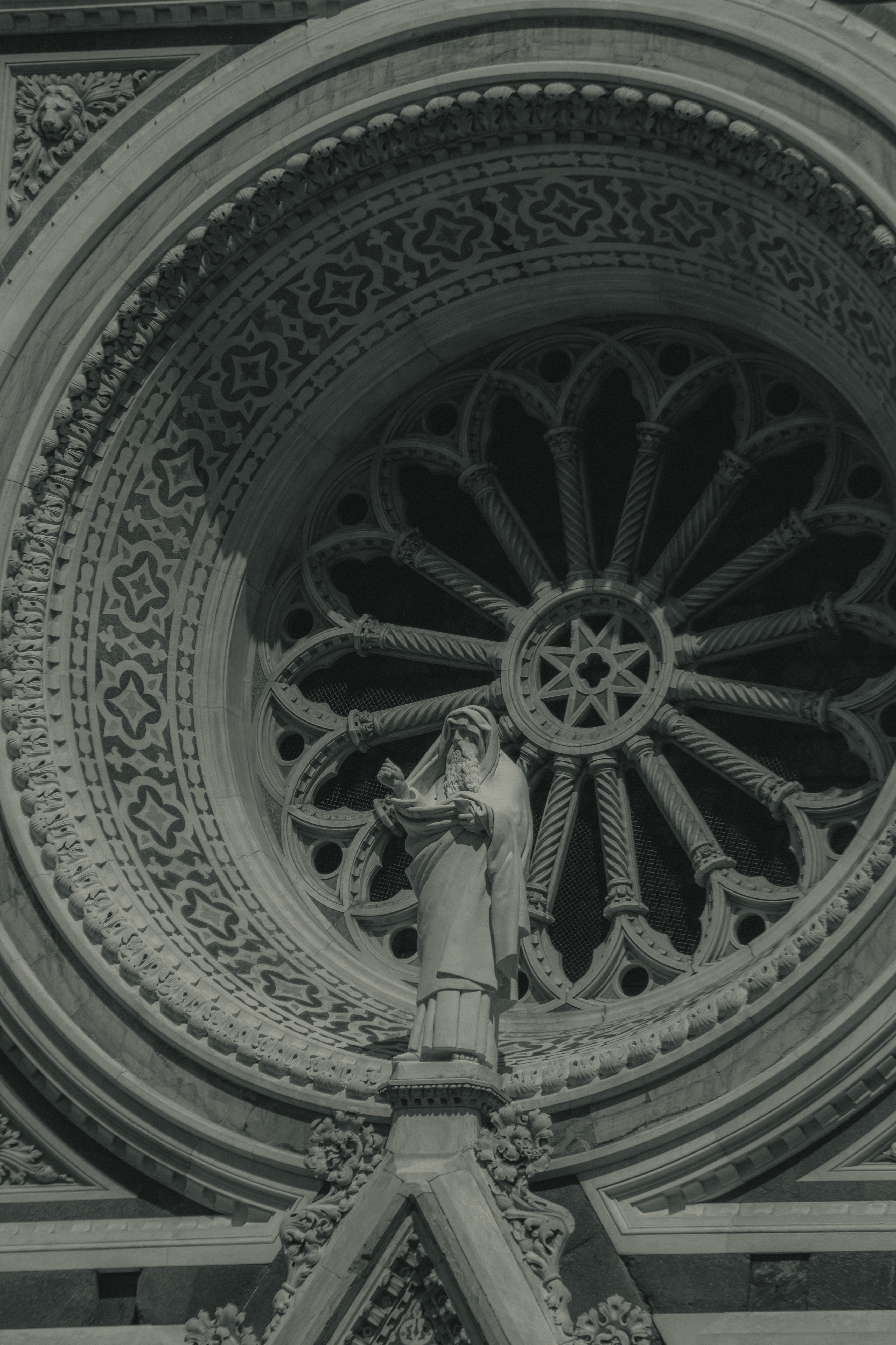Close-up of a statue and circular window detail on Florence Cathedral, showcasing Gothic architecture.