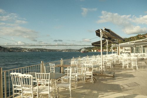 Free A serene outdoor café with white chairs and tables by the Bosphorus Bridge in İstanbul, Türkiye. Stock Photo