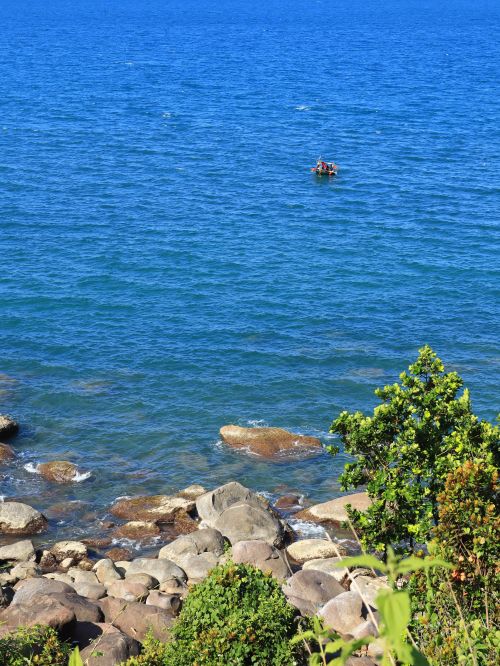 Free A tranquil scene of a lone boat on the vibrant blue sea near a rocky shoreline. Stock Photo