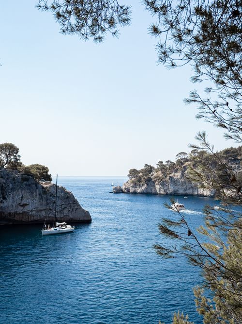 Free Tranquil coastal scene featuring a sailboat in a serene bay surrounded by cliffs and trees. Stock Photo