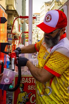 Bearded street vendor fills cup with vibrant drink from a retro pump.