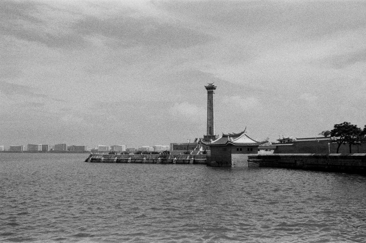 monochrome view of a riverfront featuring a traditional tower and arch