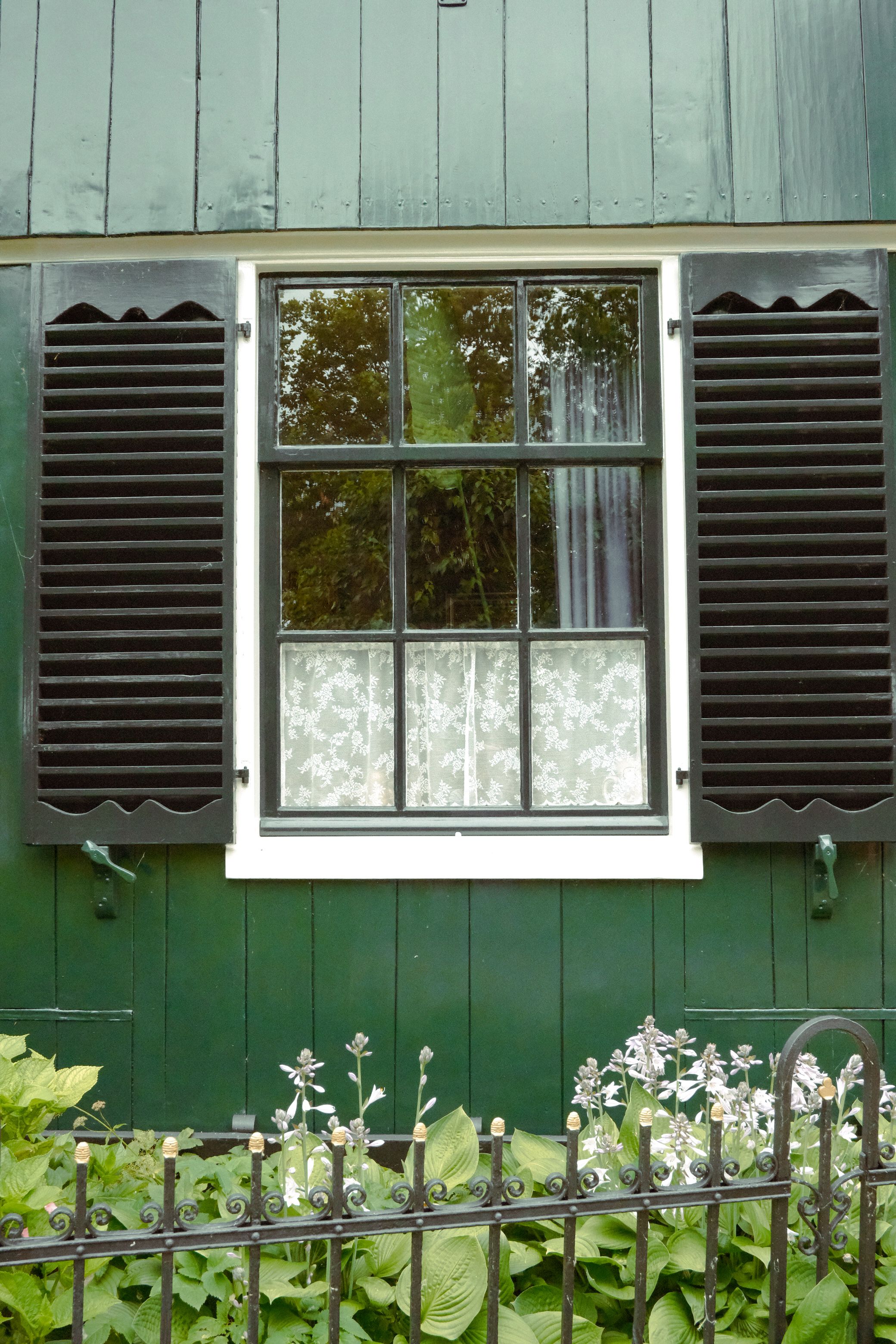 Classic green Dutch window with shutters, reflecting a serene garden in Zaandam, Holland.