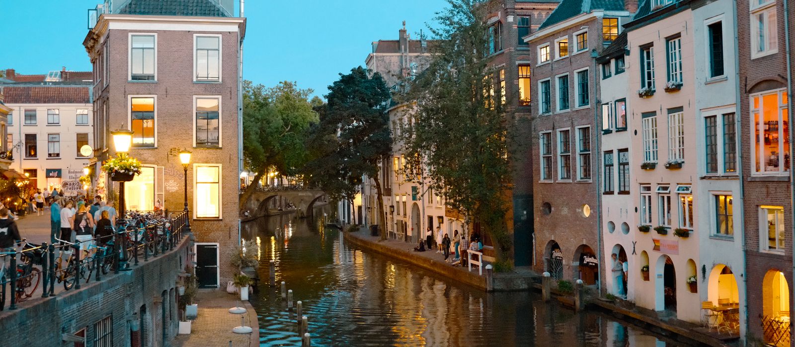 Charming night scene of Utrecht canal with historic buildings and lively social atmosphere.