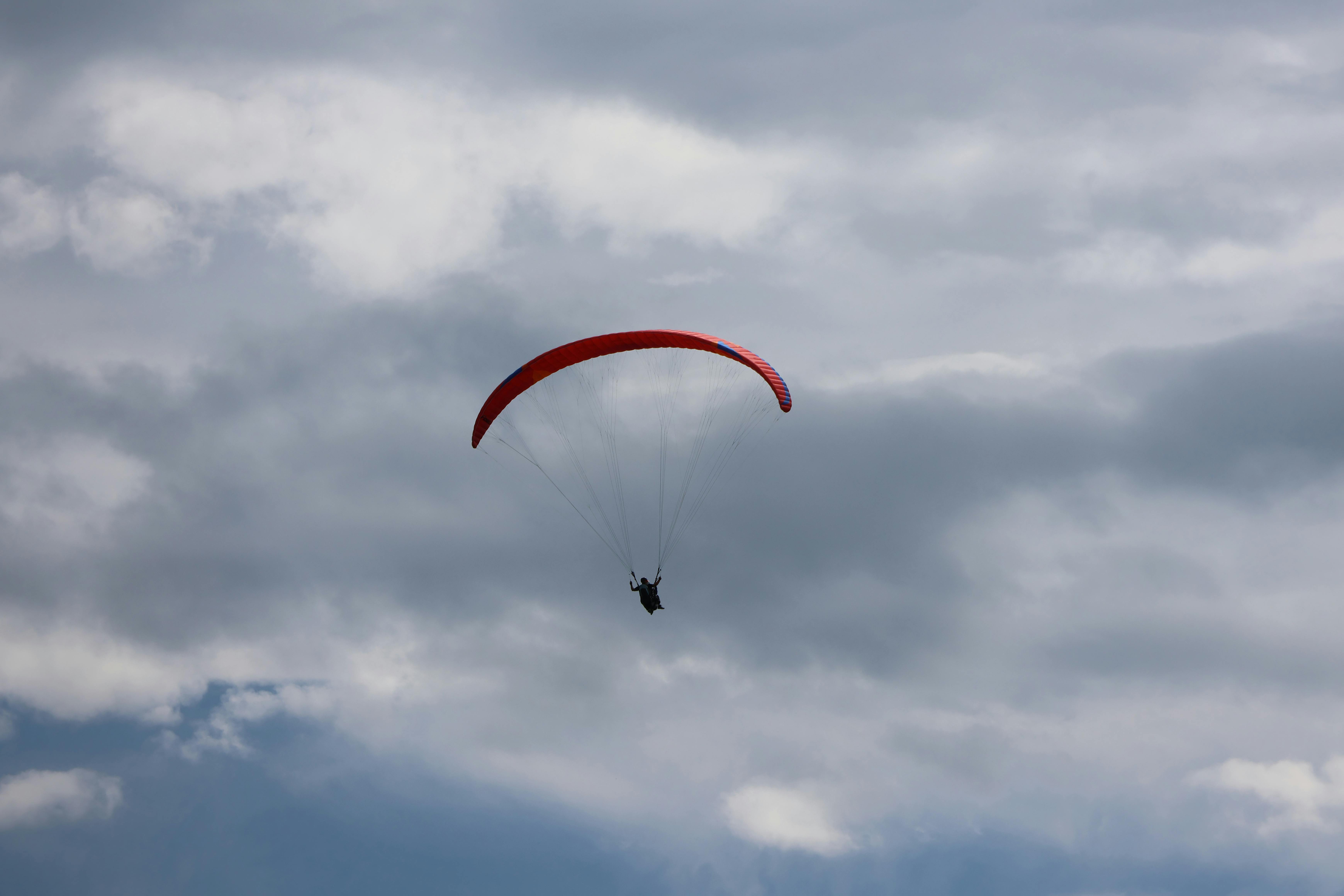 A single paraglider soars under a cloudy sky, showcasing adventure and freedom.