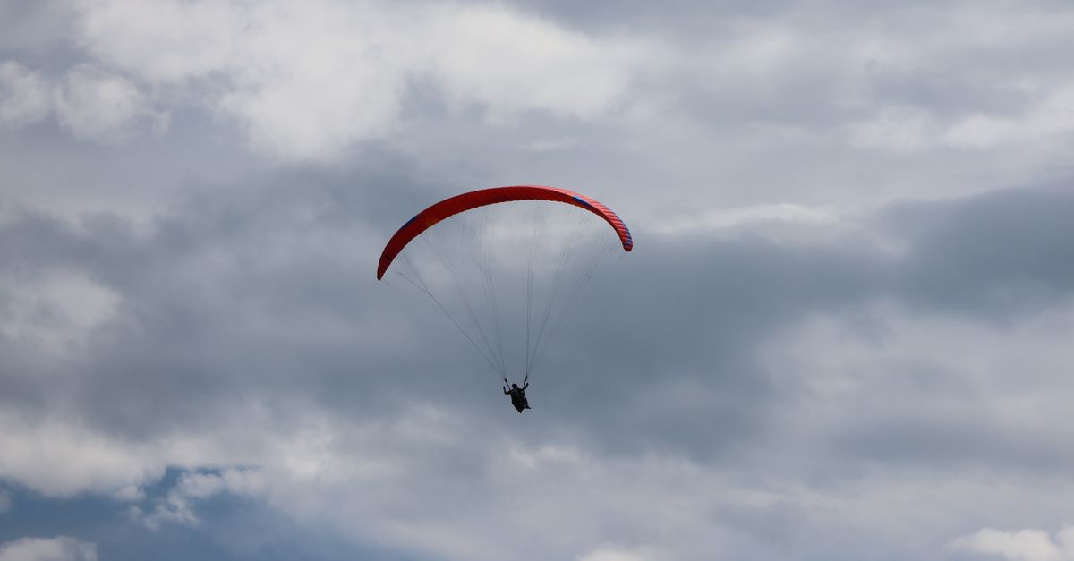 A single paraglider soars under a cloudy sky, showcasing adventure and freedom.