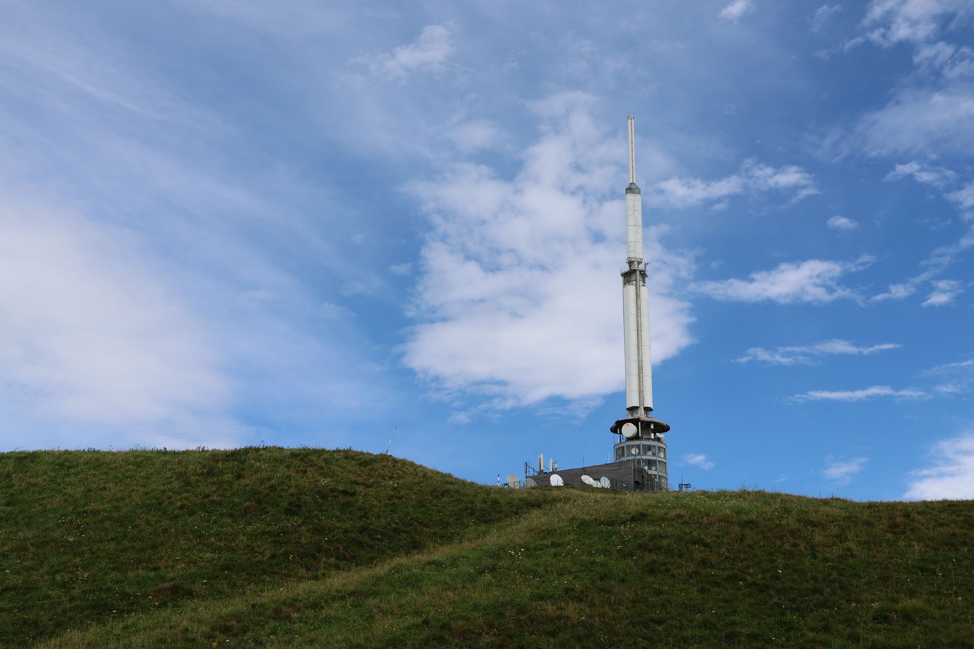 A solitary telecommunication tower stands tall on a grassy hill against a vibrant blue sky.