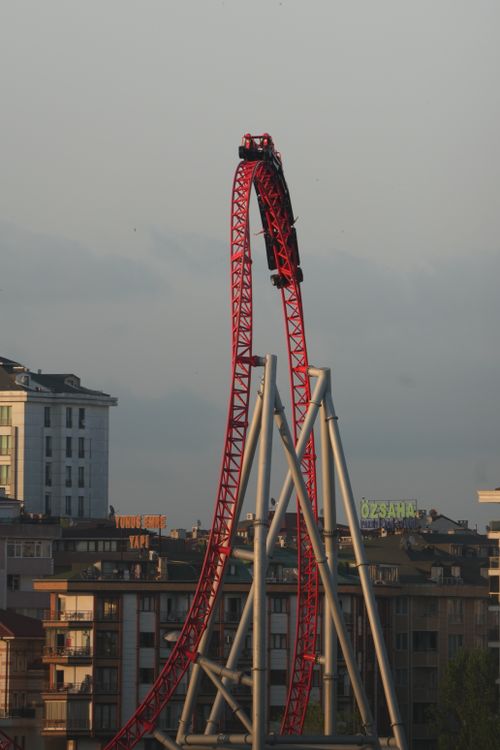 Free A vibrant red roller coaster plunges downward against a city skyline, capturing the thrill of amusement parks. Stock Photo
